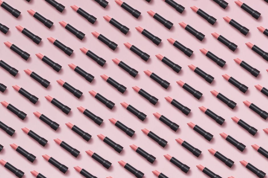Flat lay of pink lipsticks arranged in a geometric pattern on pastel background.