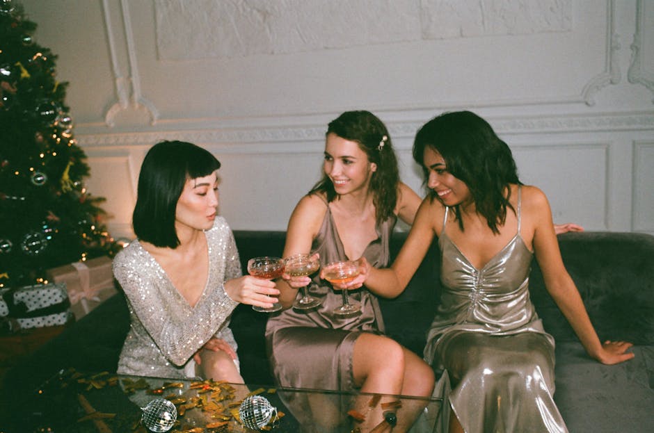 Three friends in glamorous dresses sharing drinks at a festive indoor gathering.