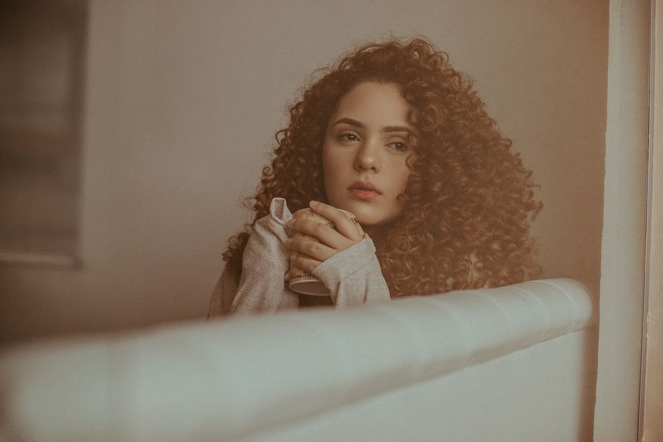A thoughtful woman with curly hair sitting indoors in a moody setting.