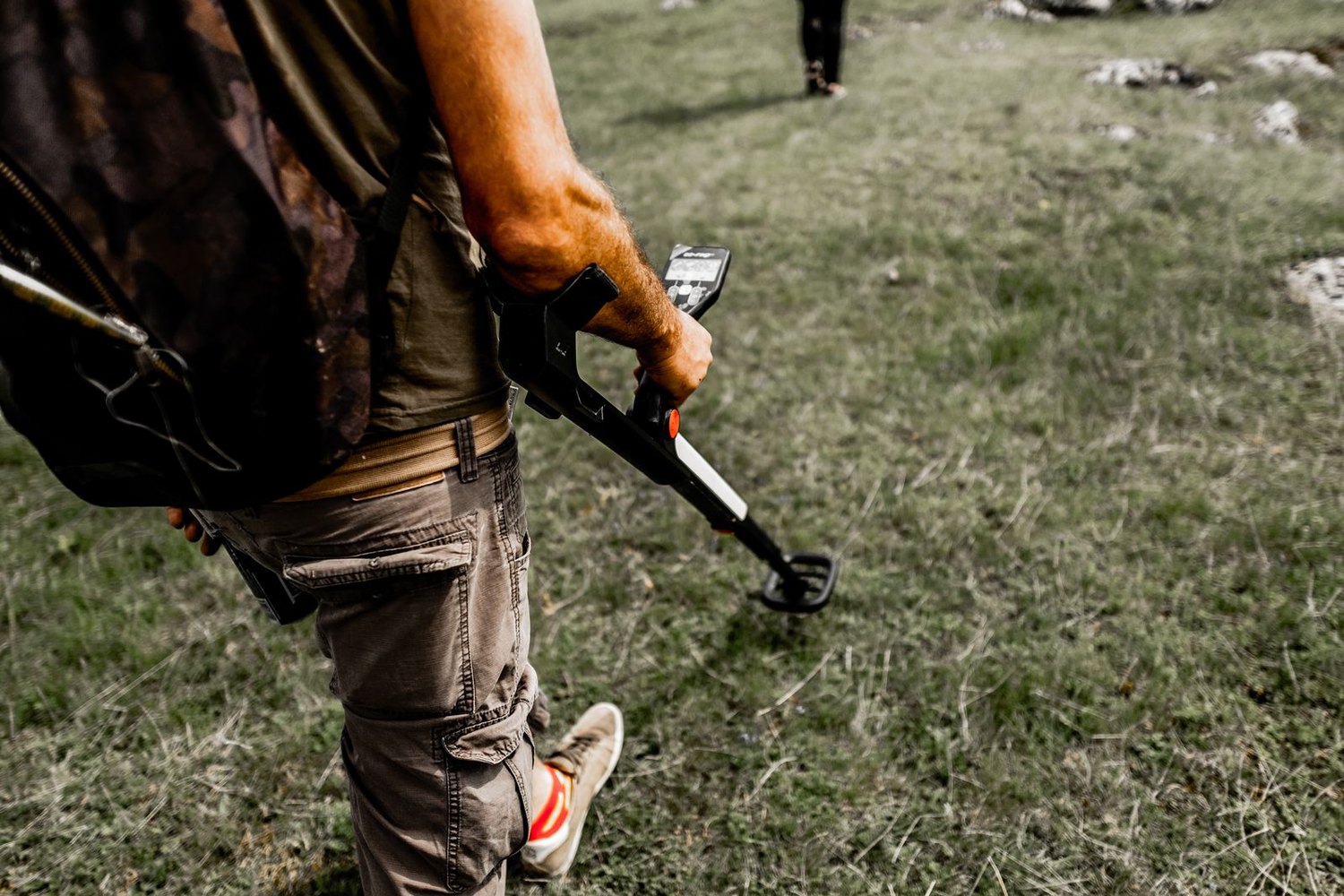 Prospector sweeping a metal detector over the ground while carrying field gear
