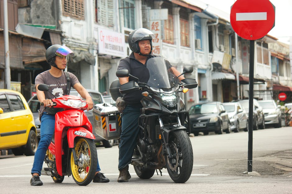 Motorcyclists on a red and black bike stopped at a city intersection with a no entry sign.