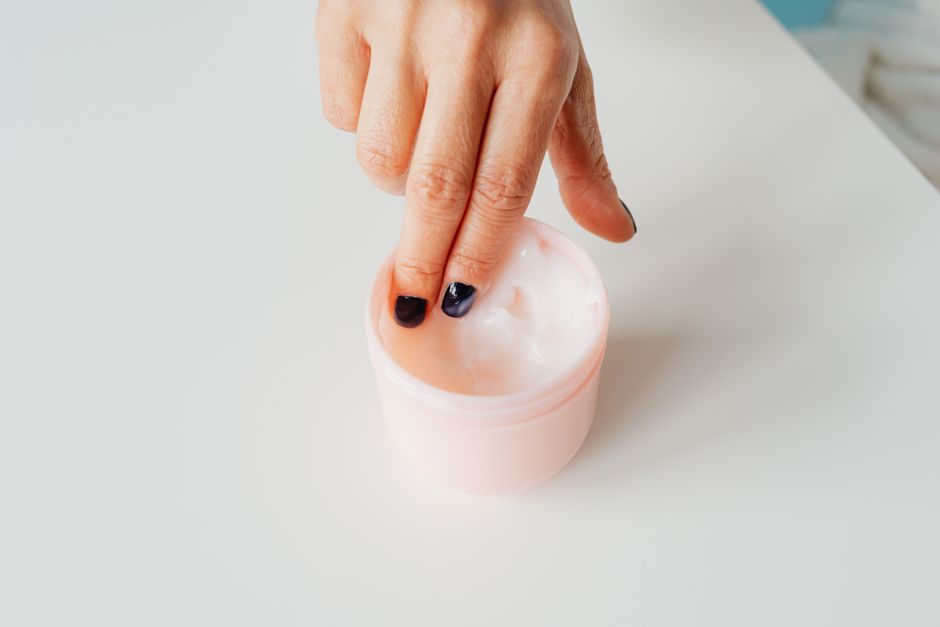 Close-up of a hand with painted nails dipping into a jar of face cream, representing self-care.