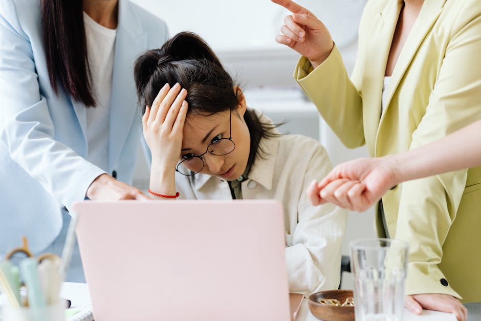 Businesswoman under pressure during an office meeting with colleagues gesturing at a laptop.